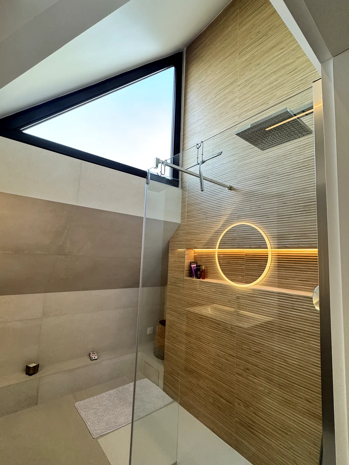 Douche à l'italienne sous la fenêtre triangulaire, mur bois rainuré et niche LED