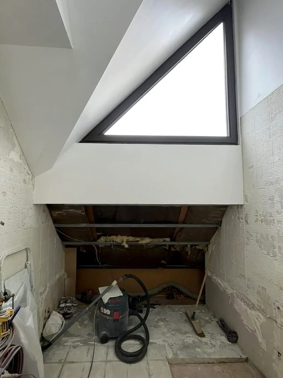 Avant travaux : combles bruts, ancien carrelage et rampant ouvert sous la fenêtre triangulaire