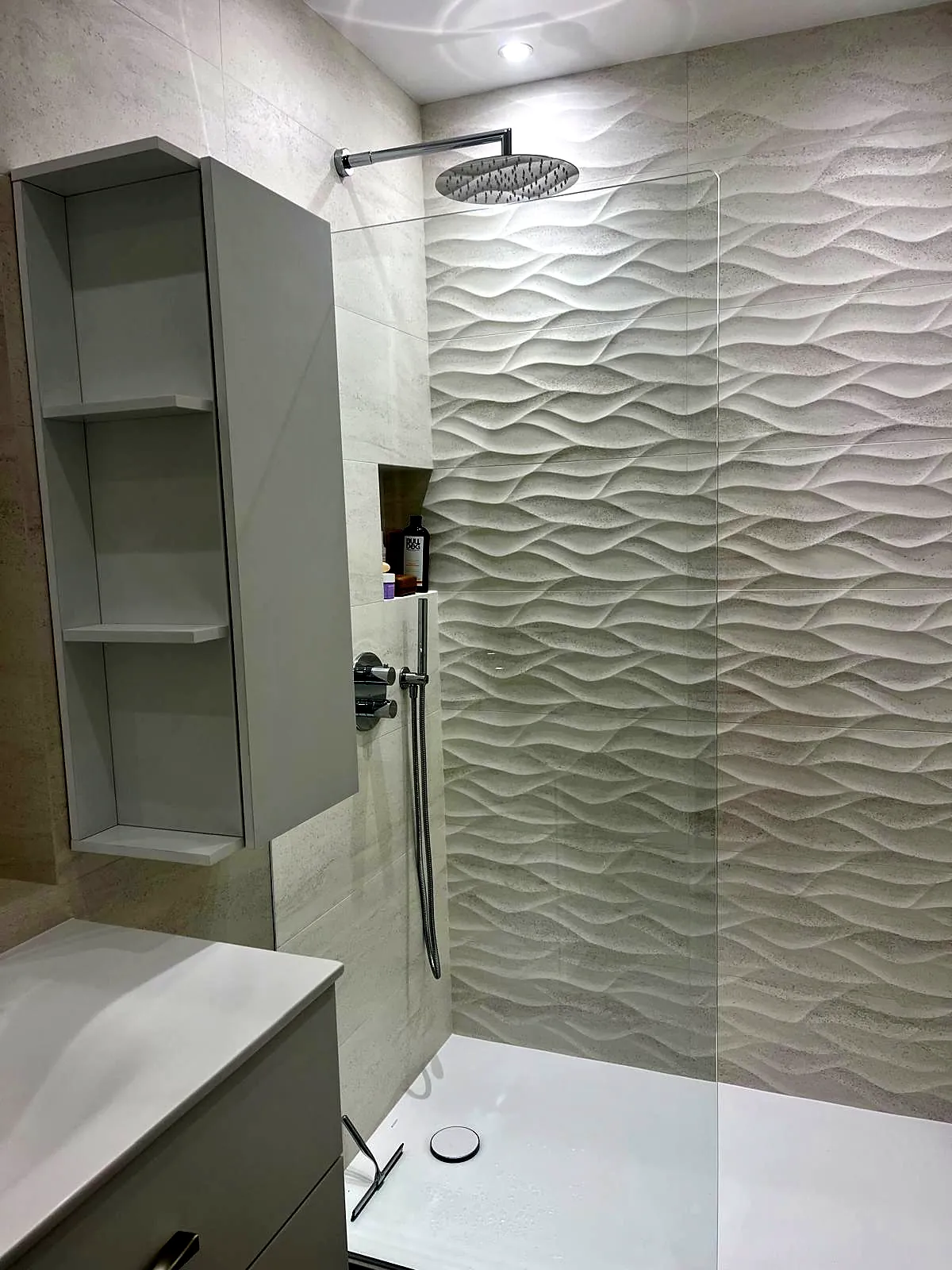 Douche à l'italienne avec faïence blanche ondulée, colonne de rangement et pommeau de tête
