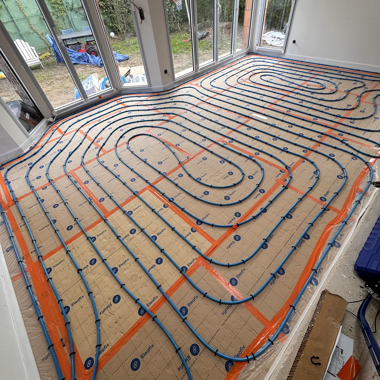 Plancher chauffant hydraulique : boucles en spirale posées sur isolant dans une véranda